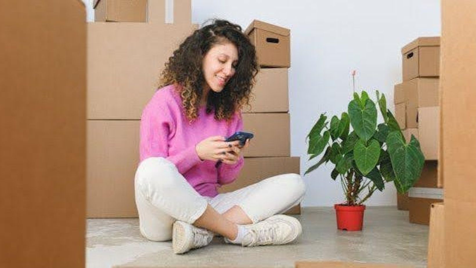 A woman sitting amid boxes and using her phone. 