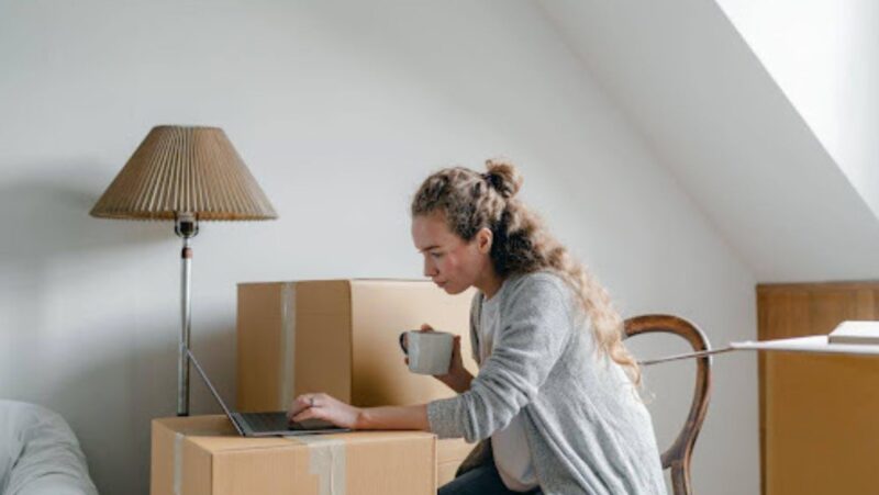 Woman looking at her laptop while surrounded by cardboard boxes